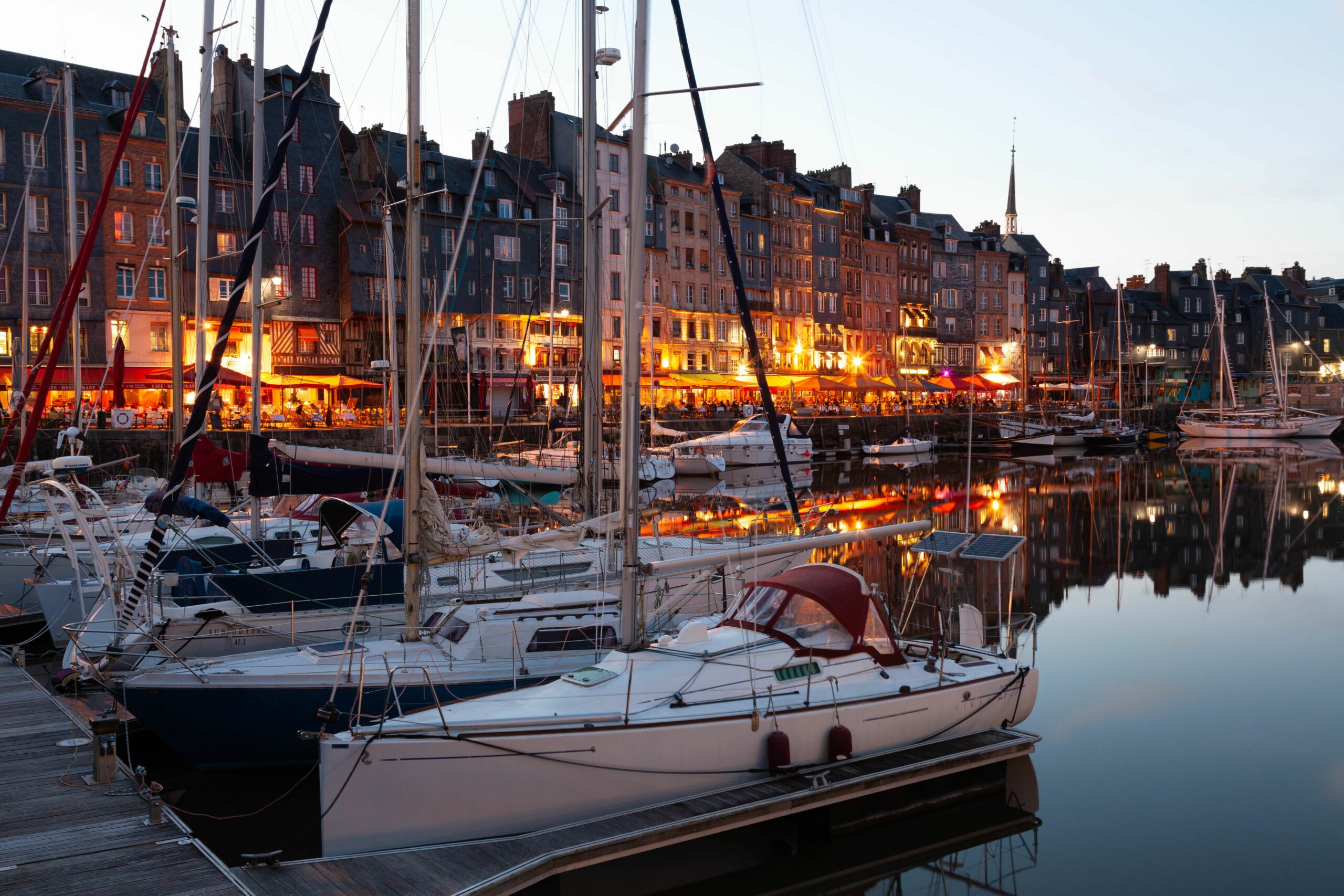 Beautiful evening view of yachts moored in Honfleur harbor reflecting colorful buildings.